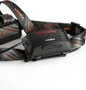 Close-up of a black headlamp with an orange and gray patterned strap. Podgląd zdjęcia produktu