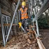 A construction worker is using a leaf blower to clear debris from a wooden platform next to a building under construction. Podgląd zdjęcia produktu