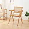 A wooden chair with a rattan back is placed in a room with a side table and a plant. Produktbild-Vorschau