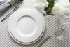 A place setting with a white plate, cutlery, and a glass on a striped tablecloth, with white flowers in the background. Produktbild-Vorschau