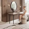A woman is sitting at a vanity table in a bedroom, applying makeup. Produktbild-Vorschau