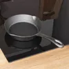 A cast iron frying pan sits on a black glass stovetop, with a wooden cutting board in the background. Produktbild-Vorschau