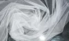 A close-up, top-down view of white tulle fabric, draped and folded to create a swirling pattern. Produktbild-Vorschau
