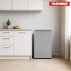 A small, silver refrigerator is shown in a kitchen setting next to white cabinets. Produktbild-Vorschau