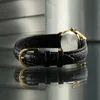 A close-up side view of a black leather watchband with a gold buckle, reflecting on a dark surface. Produktbild-Vorschau