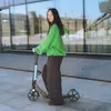 A young woman is standing on a scooter in front of a modern building. Voir les images du produit