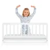 A young girl is standing behind a white bed rail. Produktbild-Vorschau