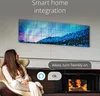 A woman sits in a chair looking at a wall-mounted LED panel displaying a colorful abstract image. A fireplace is visible to the right. Náhľad obrázku produktu