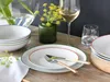 A table setting with plates, bowls, cutlery, a glass of white wine, and a small vase of yellow flowers. Produktbild-Vorschau