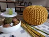 A knitted pouf and decorative items are arranged on a rug in a room. Produktbild-Vorschau