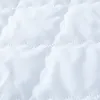 A close-up view of white quilted fabric with a scalloped edge pattern. Náhled obrázku produktu