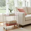 A white rolling cart with two shelves, holding books and folded blankets, is placed next to a cream-colored sofa with a pink pillow. Anteprima dell’immagine prodotto
