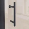A close-up of a black shower door handle against a tiled wall. Produktbild-Vorschau