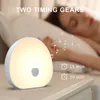 A bedside lamp is shown on a nightstand next to a sleeping person, with musical notes and text overlay indicating features. Produktbild-Vorschau