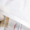 A close-up of a white sheer curtain with a satin ribbon overlay, partially covering an image of a cake and a cup of tea. Produktbild-Vorschau