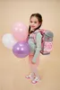 A young girl is posing with a backpack and balloons. Produktbild-Vorschau