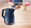A dark blue Tefal kettle with copper accents is placed on a wooden table, with a blurred background showing someone preparing breakfast. Produktbild-Vorschau