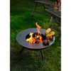 A fire pit with food cooking on it, set on a grassy lawn with outdoor furniture in the background. Produktbild-Vorschau
