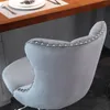Close-up of the back of a gray velvet bar stool with silver stud detailing, placed near a wooden countertop with a plate and cutlery. Produktbild-Vorschau
