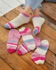 A pair of feet wearing socks on a wooden surface, with several other pairs of socks laid out. Produktbild-Vorschau