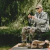 A person is sitting on a folding stool by a body of water, holding a fishing rod. Produktbild-Vorschau
