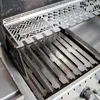 A close-up view of a stainless steel grill with a metal heat shield placed over the grates. Produktbild-Vorschau