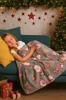 A young girl sleeps on a couch, covered by a Christmas-themed blanket, with a decorated Christmas tree and wall decorations in the background. Náhled obrázku produktu