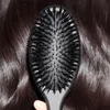 A close-up of a black hairbrush with nylon bristles against a background of dark brown hair. Produktbild-Vorschau