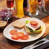 A partially assembled burger and fries on a plate, with drinks and condiments in the background. Produktbild-Vorschau