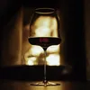 A glass of red wine sits in front of a fireplace. Produktbild-Vorschau