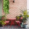 A red metal bistro set with two chairs and a table on a balcony with plants. Náhľad obrázku produktu