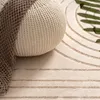 A close-up view of a textured pouf and a rug with a geometric pattern. Produktbild-Vorschau