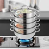A multi-tiered stainless steel steamer pot filled with food, placed on a gas stove with a blue flame. Podgląd zdjęcia produktu