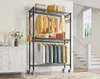 A rolling garment rack filled with clothing and accessories, placed in a room with a white dresser and stairs in the background. Voir les images du produit