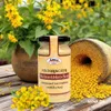 A jar of mustard is placed on a wooden table next to a pot of yellow flowers and a stone mill with mustard seeds. Náhľad obrázku produktu