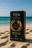 A large tin of olive oil sits on a sandy beach with the ocean in the background. Produktbild-Vorschau