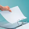 A hand is inserting a white sheet of paper into a white binder with silver rings. Produktbild-Vorschau