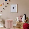 A child's room with a pink storage ottoman, a wicker chair with stuffed animals, and a framed picture on the wall. Podgląd zdjęcia produktu