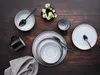 A top-down view of a table setting with plates, bowls, mugs, and cutlery, along with a small vase of flowers. Náhľad obrázku produktu