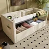 A beige upholstered sofa bed with storage, showing folded linens and pillows inside. Produktbild-Vorschau