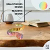 A colorful, segmented snake toy is coiled on a wooden table in front of an open book. The background is blurred. Voir les images du produit