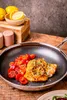 A close-up of a pan with food, with lemons and salt and pepper shakers in the background. Náhled obrázku produktu
