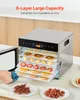 A person's hand is shown opening the door of a stainless steel food dehydrator filled with various dried fruits and jerky. Two plates of dried food are on the counter in front of the dehydrator. Podgląd zdjęcia produktu