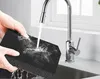 Hands holding a black sponge under running water from a kitchen faucet. Voir les images du produit