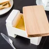 A butter dish with a wooden lid sits on a dark surface, with toast and a knife nearby. Podgląd zdjęcia produktu
