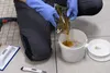 A person wearing blue gloves is pouring a yellow liquid from a pouch into a white bucket. Podgląd zdjęcia produktu