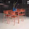 A terracotta colored metal garden table and four chairs are set up in a modern cafe or restaurant setting with a black tiled wall in the background. Anteprima dell’immagine prodotto