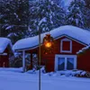 A lantern hanging from a garden hook in a snowy setting with red houses in the background. Produktbild-Vorschau