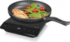 A frying pan with chicken and vegetables is placed on a black induction hob. Voir les images du produit