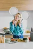 A woman is in a kitchen holding two frying pans over her shoulders. Produktbild-Vorschau